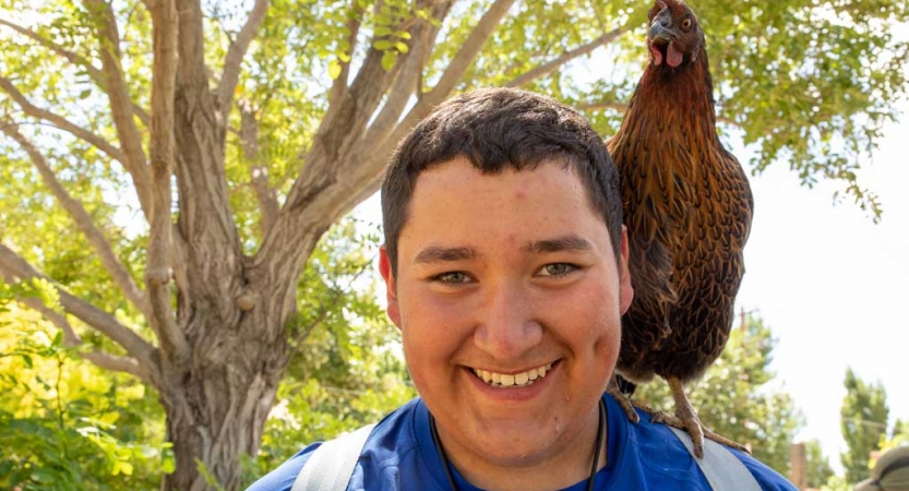A person smiles at the camera, with a chicken perched on their shoulder.